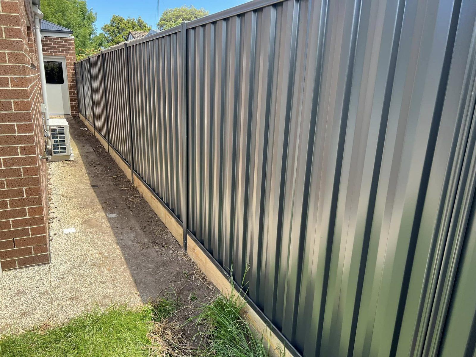 Charcoal Colorbond fence with a timber plinth along a driveway